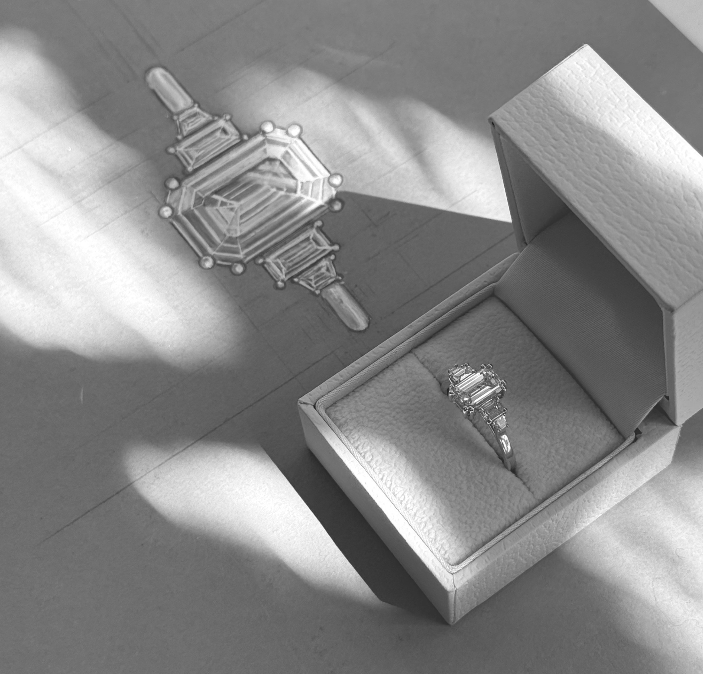 Skitse af emerald cut ring ved siden af smykkeæske med den færdige ring
